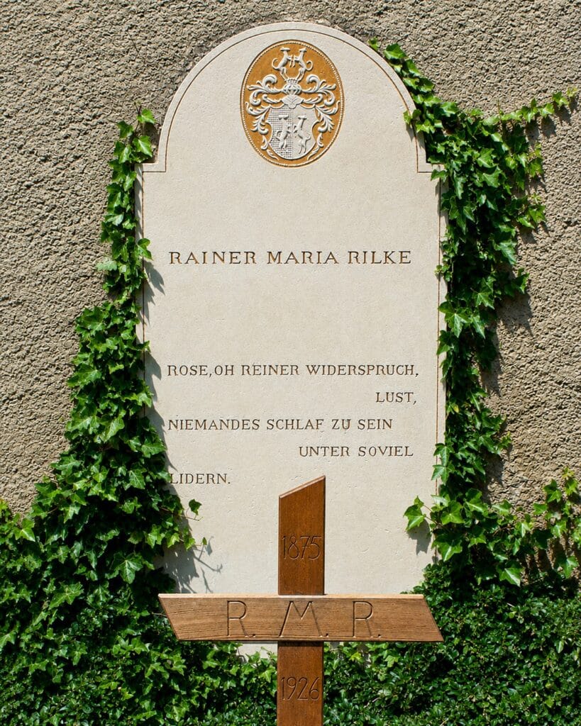 Front view of Rainer Maria Rilke's gravestone beside the south wall of St. Romanus Church in Raron, showing his name and the rose epitaph he chose.