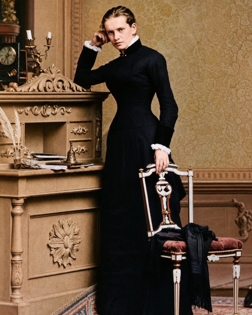 Full-length studio portrait of the young Lou Andreas-Salomé standing beside an ornate desk, years before she met René Maria Rilke and encouraged him to use the name Rainer.